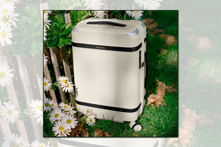 Paravel Aviator Carry-On Plus on grass next to a fence with daisies